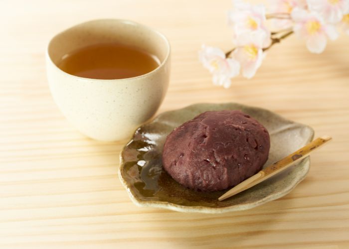 A serving of ohagi mochi next to a cup of traditional Japanese tea. The mochi is served on a leaf-shaped plate.